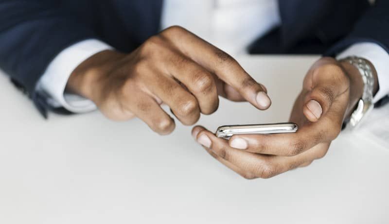 Vyras juodu kostiumu, laikantis išmanųjį telefoną