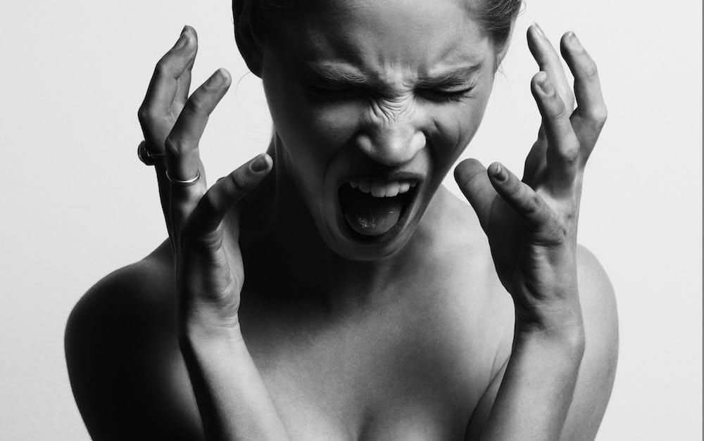 Fotografía en escala de grises de una mujer abriendo la boca mientras cuelga las manos cerca de su rostro