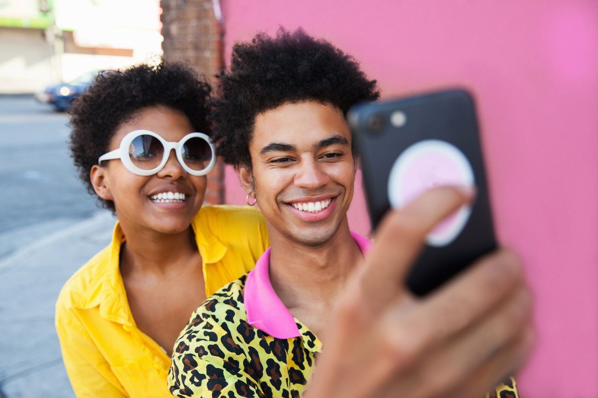 Una joven pareja vistiendo ropa amarilla tomando un selfie delante de una pared rosa.