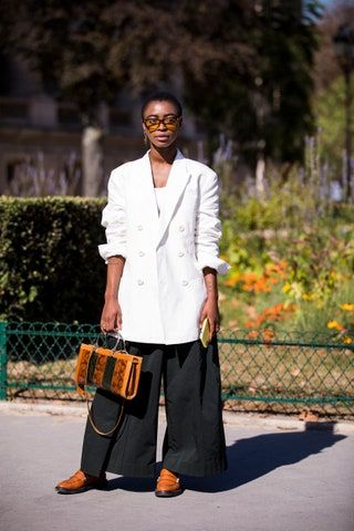 Un invitado con un blazer largo blanco, pantalones negros, mocasines naranjas y un bolso con estampado de serpiente, se ve antes del desfile de Paco Rabanne.
