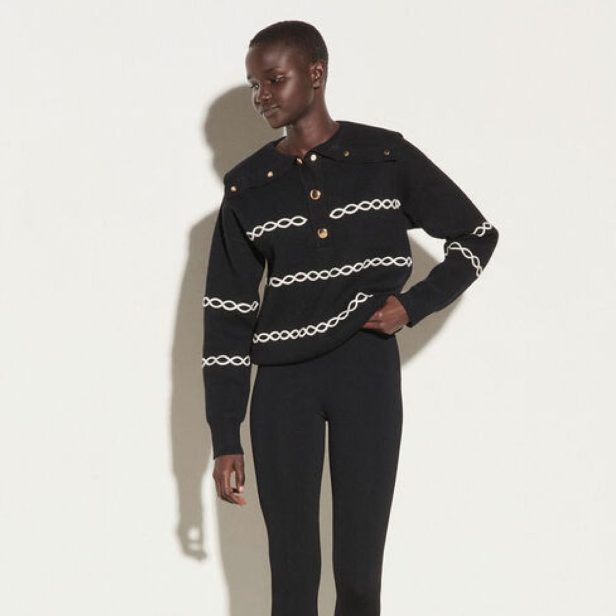 modelo vistiendo un suéter negro con rayas y botones de cadena blanca