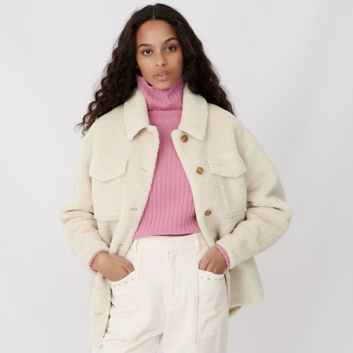 Modelo vistiendo chaqueta blanca borrosa sobre cuello alto rosa con pantalones blancos