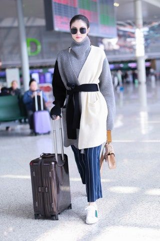 スイ彼は空港に大きなセーターとストライプのズボンを着ています