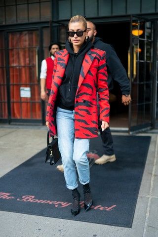 Mujer vistiendo un abrigo de rayas de cebra roja sobre una sudadera con capucha negra y jeans azules