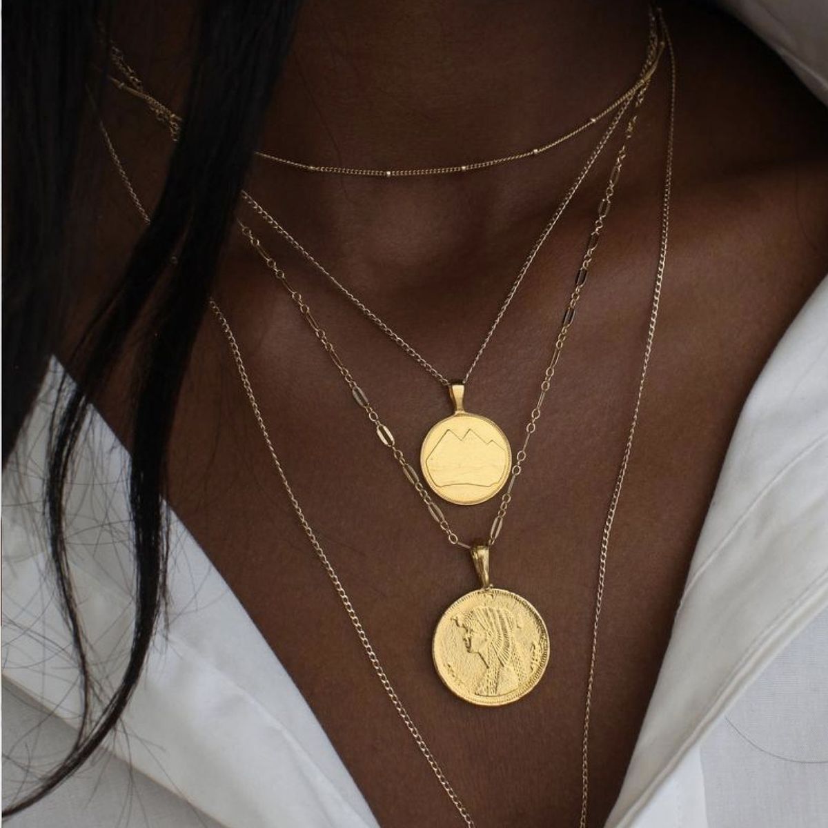 modelo con collares de oro apilados con amuletos de monedas planas