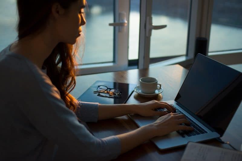 Mujer escribiendo en su computadora portátil durante el anochecer